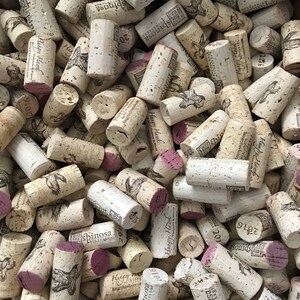 May include: A close-up of a pile of wine corks with various labels and dates. The corks are mostly brown and beige with some having a pink or purple hue. The labels include the names "Hungry Hawk", "Spinosa Vineyards", and "Esponda".