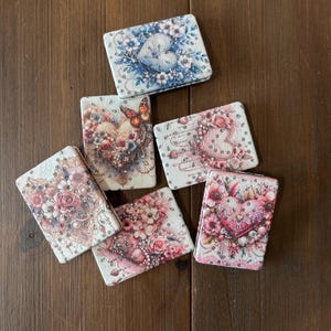 May include: Six rectangular compact mirrors featuring intricate designs of hearts, flowers, and butterflies in shades of blue, pink, and cream. Each mirror is embellished with small, reflective circular accents that mimic the appearance of rhinestones.