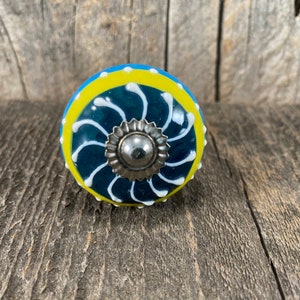 May include: A blue and yellow ceramic knob with a white swirl design and a silver metal center.