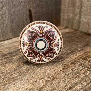 Pode incluir: Um botão de cerâmica branco com um design floral rosa, marrom e azul. O botão tem uma borda dourada.