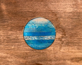 May include: Oval-shaped ring with a blue and white striped inlay. The ring is made of metal and has a polished finish.