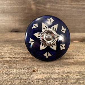 May include: A blue ceramic knob with a white floral design and a silver metal centre.