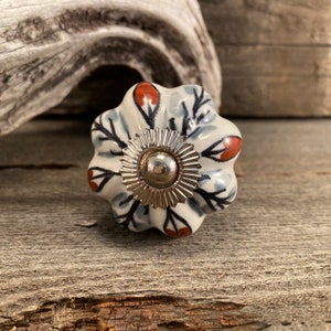 Peut inclure: Un bouton en céramique blanche avec un centre en métal argenté. Le bouton a un motif floral avec des accents rouges et noirs.