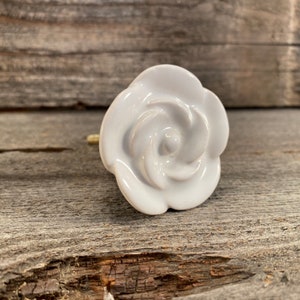 May include: White ceramic rose-shaped drawer pull. The rose has a swirl design and is a simple, elegant design.