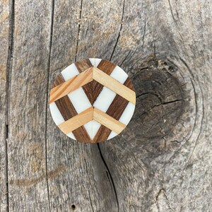 Puede incluir: Perilla de armario redonda de madera con diseño geométrico. La perilla presenta secciones alternas de madera clara, madera oscura y resina blanca, creando un patrón atractivo. Ideal para muebles y decoración del hogar.