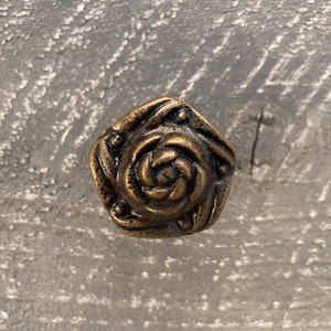 May include: A gold-toned metal cabinet knob with a rose design. The knob has a hexagonal shape and a raised, detailed rose in the center.
