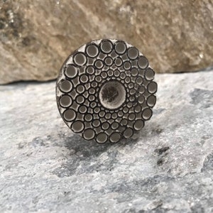 May include: A round, white ceramic knob with a concentric circle design. The knob has a raised, textured surface with a circular pattern.