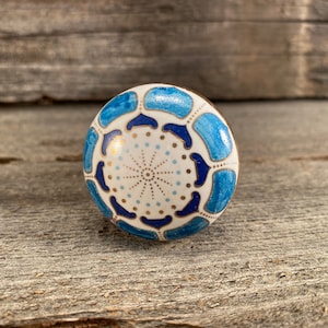 May include: A white ceramic knob with a blue and gold geometric pattern. The knob has a round shape and is perfect for adding a touch of style to any room.