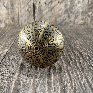 May include: A round, black and gold decorative knob with an intricate floral pattern.