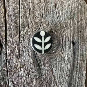 May include: A black and white ceramic knob with a stylized floral design. The knob is round and has a smooth surface.