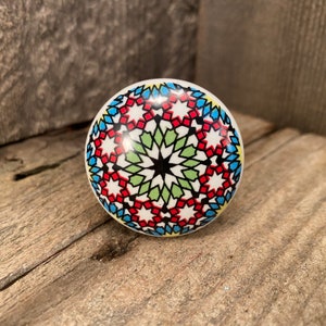 May include: A round ceramic knob with a colorful geometric pattern in shades of blue, red, green, and black. The pattern features a starburst design.