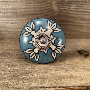 May include: A blue ceramic knob with a white floral design and a silver metal center.