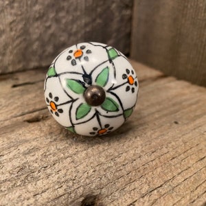 May include: White ceramic knob with a green and orange floral pattern. The knob has a metal base.