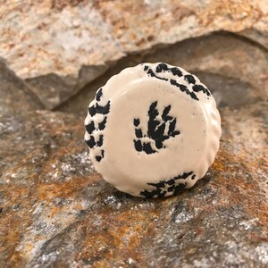 Może przedstawiać: Biały ceramiczny gałka z czarnym wzorem kwiatowym. Gałka ma podniesiony brzeg i gładką powierzchnię.