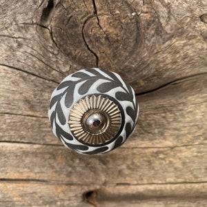 May include: Black and white ceramic knob with a silver center and a leaf pattern.