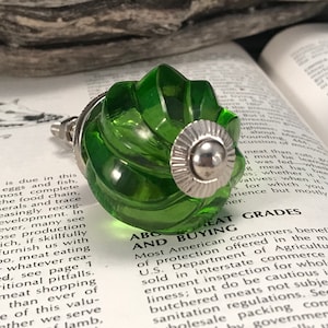 May include: A green glass cabinet knob with a silver metal base. The knob has a swirl design and a raised, circular center.