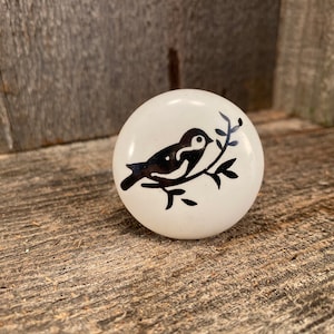 May include: White ceramic knob with a black silhouette of a bird perched on a branch.