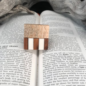 Puede incluir: Un primer plano de un bloque de madera con un patrón de rayas blancas y marrones. El bloque está hecho de diferentes tipos de madera, incluyendo una madera marrón claro con un patrón de grano y una madera marrón oscuro con un acabado liso. El bloque es un elemento decorativo que se puede utilizar de diversas maneras, como un pisapapeles o un sujetalibros.