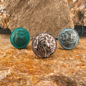 以下が含まれることがあります： 花柄の装飾的なキャビネットノブが3つ。ノブはターコイズ、白、ライトブルーに塗られています。