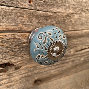 May include: A blue ceramic cabinet knob with a silver metal base and a black floral design.