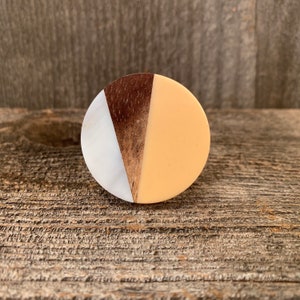 May include: A round wooden knob with a white, brown, and peach design. The knob is made of wood and has a smooth finish.