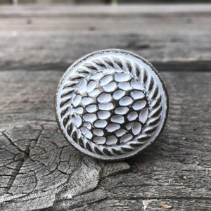 May include: White ceramic cabinet knob with a rope design around the edge and a textured centre.