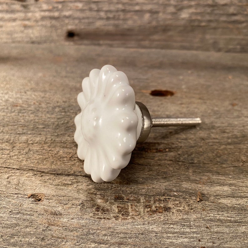 Pu&ograve; includere: Pomello per armadio a forma di margherita in ceramica bianca con vite color argento. Il pomello ha una finitura lucida ed &egrave; posto su una superficie di legno stagionato. Questo hardware decorativo &egrave; adatto per cassetti e armadi.
