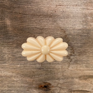 May include: A white ceramic drawer pull with a flower design. The pull has a raised centre and a scalloped edge.