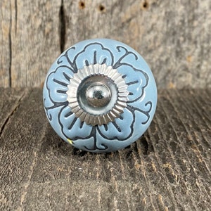 Könnte beinhalten: Ein blauer Keramik-Knopf mit einem silbernen Metallzentrum und einem floralen Design.