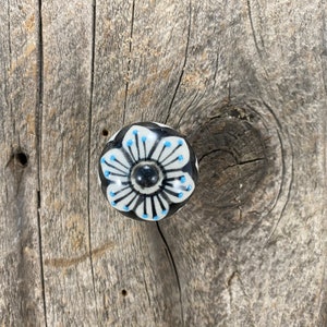 May include: A white ceramic knob with a black and blue floral design. The knob is round and has a raised design.