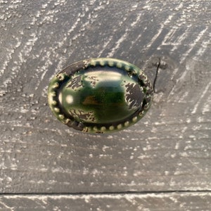 Könnte beinhalten: Ein grüner, ovaler Schrankknopf mit einem perlenbesetzten Rand und einer abgenutzten Oberfläche.