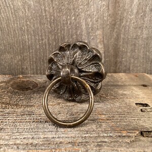 May include: A decorative metal ring pull with a floral design. The ring pull is made of a dark metal and has a rustic finish.