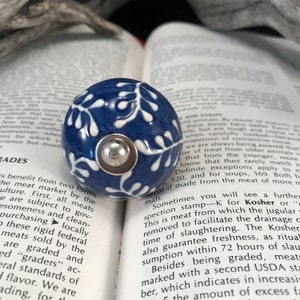 May include: A blue and white ceramic knob with a floral design. The knob is sitting on top of a book with text about Kosher meat.