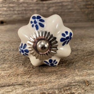Könnte beinhalten: Weißer Keramik-Knopf mit silbernem Metallzentrum und blauem Blumenmuster.