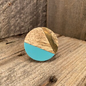 Puede incluir: Un pomo redondo de madera con un diseño geométrico azul y dorado. El pomo está hecho de madera con veta natural y tiene una sección pintada de azul con un acento dorado.