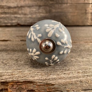 May include: A gray ceramic knob with a white floral design and a silver metal base.