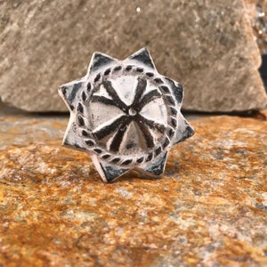 May include: A star-shaped, white and black decorative object with a central design and a surrounding rope-like border. The object is set against a textured, brown and tan stone surface.
