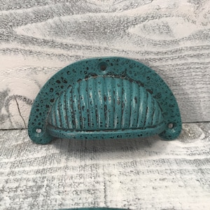 May include: A teal blue cast iron drawer pull with a ribbed design. The pull has a distressed finish and is shaped like a half-circle.
