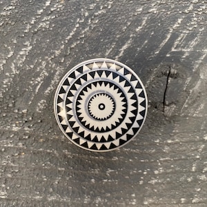 May include: Black and white ceramic knob with a geometric pattern. The knob has a circular shape with concentric circles and triangles.