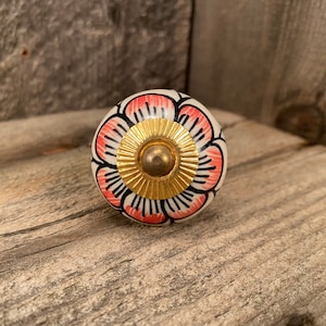 May include: A white ceramic knob with a pink and black floral design and a gold center. The knob is perfect for adding a touch of elegance to any room.