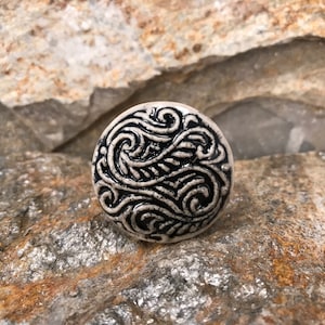 May include: A white ceramic knob with a black swirling design. The knob is round and has a smooth surface.