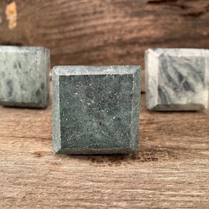 May include: Three square-shaped drawer pulls made of green and gray marble. The pulls have a smooth, polished finish.