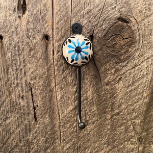 Puede incluir: Un gancho de metal negro con una perilla de cerámica blanca con un diseño floral azul y negro.