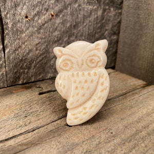 May include: A white ceramic owl figurine with detailed carving. The owl has large eyes and a textured body.