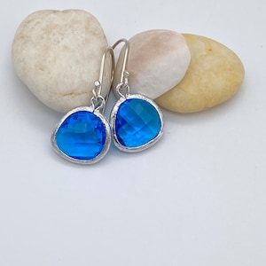 May include: A pair of silver dangle earrings with blue gemstone drops. The earrings have a simple design and are perfect for everyday wear.
