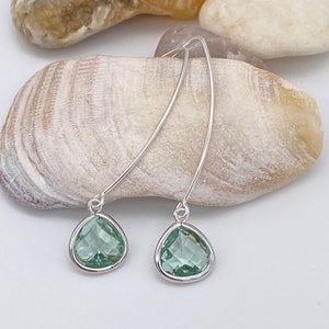 May include: A pair of silver dangle earrings with light green teardrop-shaped crystals.