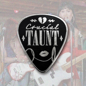 Puede incluir: Púa de guitarra negra con texto plateado que dice "Crucial Taunt" con un corazón roto y un diseño de labios plateados.
