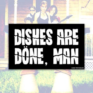 Puede incluir: Adhesivo rectangular negro con el texto "DISHES ARE DONE, MAN" en blanco, con letras agrietadas. El adhesivo tiene una estética vintage. El aviso de copyright "©2026 TAVIS BALKIN" está en la esquina inferior derecha.