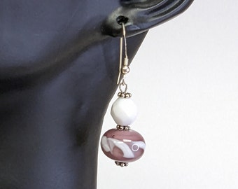 May include: Silver dangle earrings with a white and purple glass bead. The purple bead has white swirls.