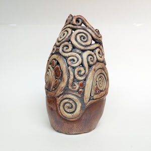 Puede incluir: Un jarrón de cerámica marrón con un diseño único de patrones en espiral y pequeños puntos rojos. El jarrón está hecho a mano y tiene una superficie texturizada.